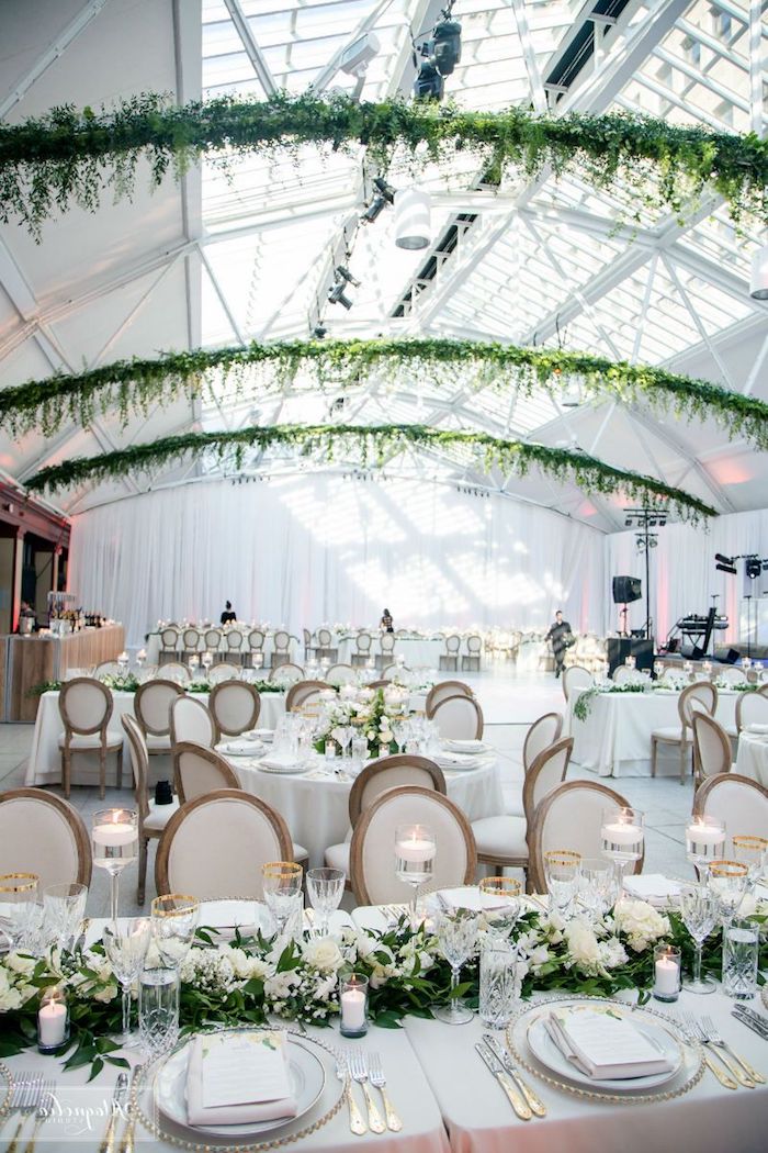 arche de feuillages en hauteur, table décorée de nappe blanche et centre de feuillages et fleurs blanches, bougies blanches, couvets or