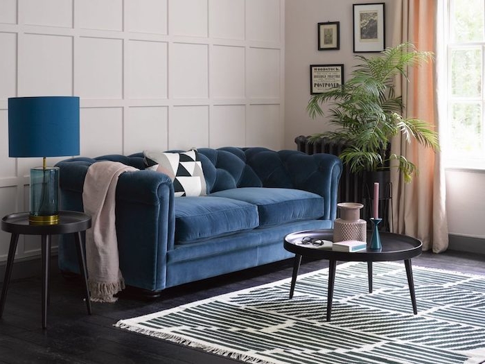canapé bleu nuit dans un salon blanc aux rideaux peche clairs, parquet bois foncé avec tapis zèbre et table basse noire