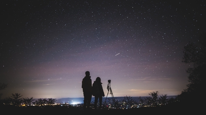 idée de sortie en amoureux originale, couple amoureux qui observe le ciel nocturne sur un colin avec une vue sur la ville