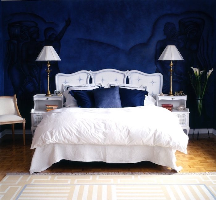 couleur bleu nuit en peinture murale à motifs silhouettes humaines, linge de lit blanc et coussins bleu nuit, parquet bois clair
