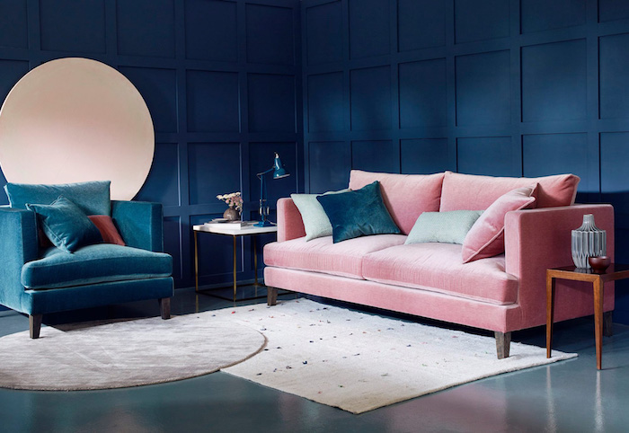 murs couleur bleu nuit, fauteuil bleu foncé et canapé rose dans un salon bleu foncé, tapis rectangle et tapis rond bleu et gris, coussins decoratifs colorés, table de service bois
