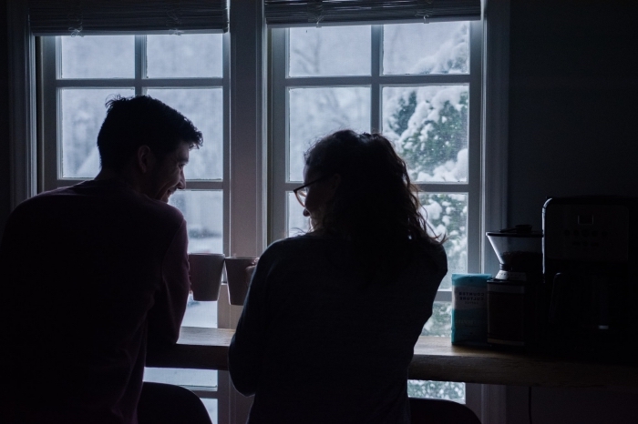 activité en couple, couple amoureux qui boivent chocolat chaud devant une grande fenêtre avec vue vers des arbres enneigés