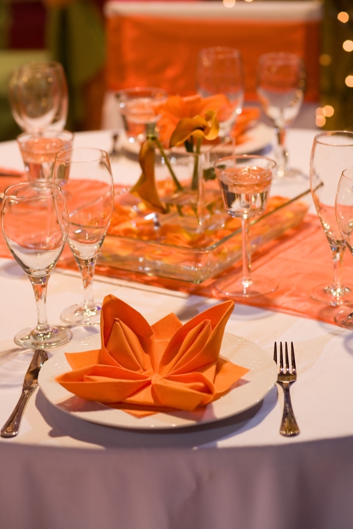 réaliser une fleur de lotus facile avec serviette en papier orange, arrangement de table stylée en blanc et orange