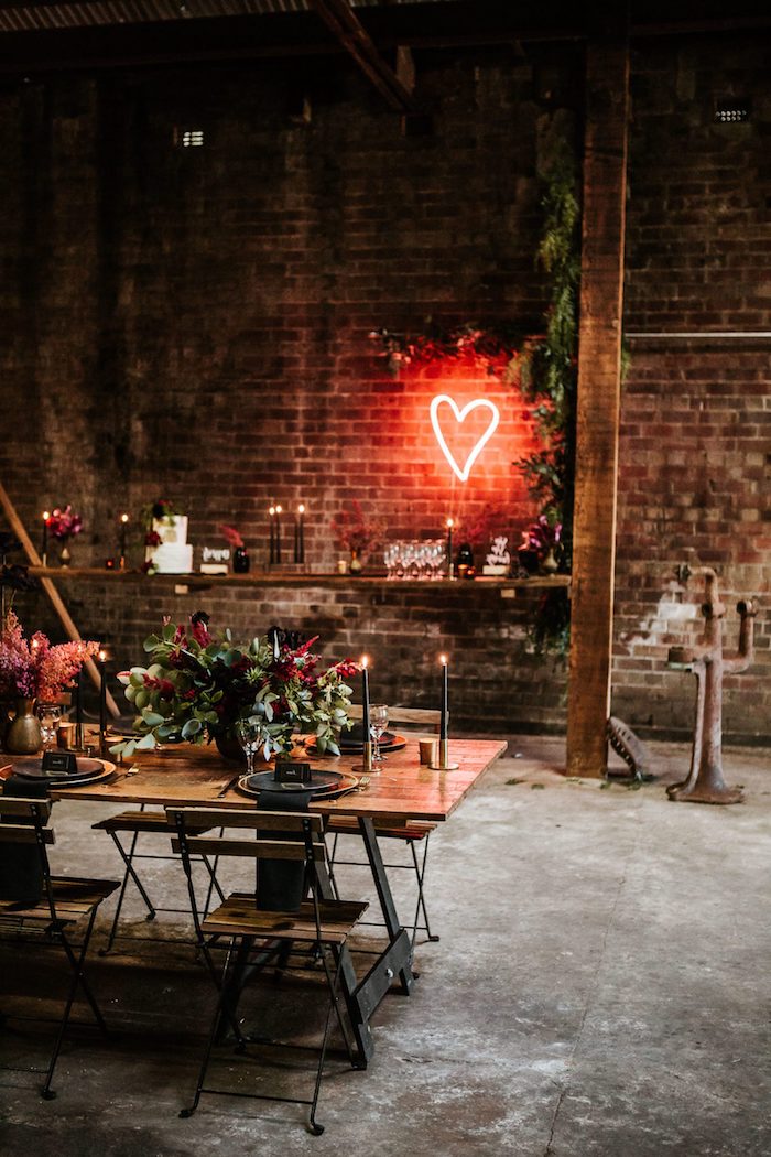 idée thème mariage industriel chic dans salle de mariage industrielle, déco coeur néon sur murs de briques, chaises et table industrielle en bois et métal, déco florale en vert et rouge