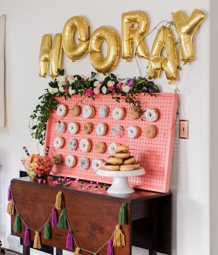 panneau perforé décoré de beignets avec decoration de guirlande de fleurs, ballons en lettres dorées, meuble candy bar bois vintage