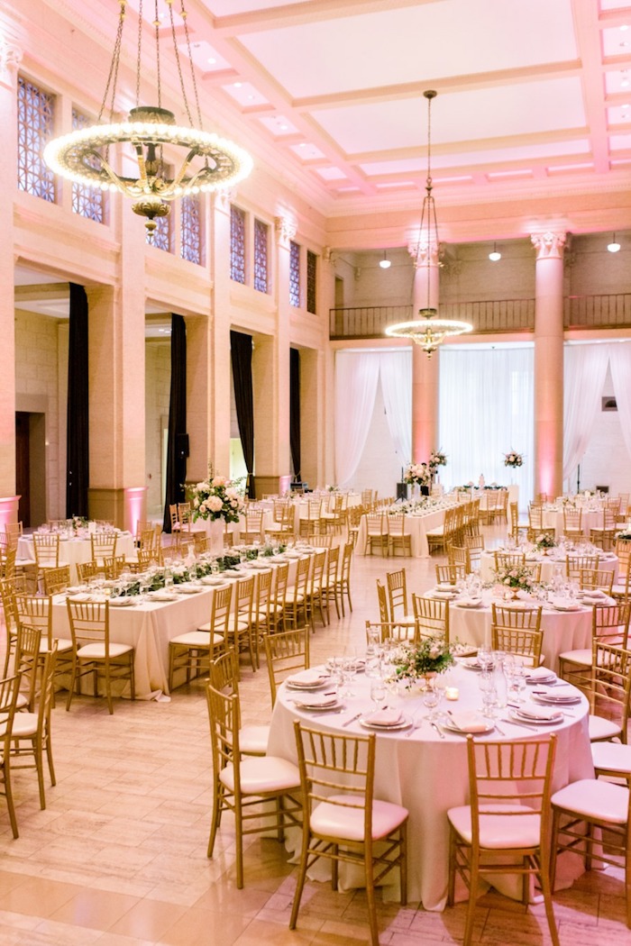 lustres avec lumières au dessus de table en nappe blanche et chaises bois et blanc, murs blancs, parquet salle de mariage clair