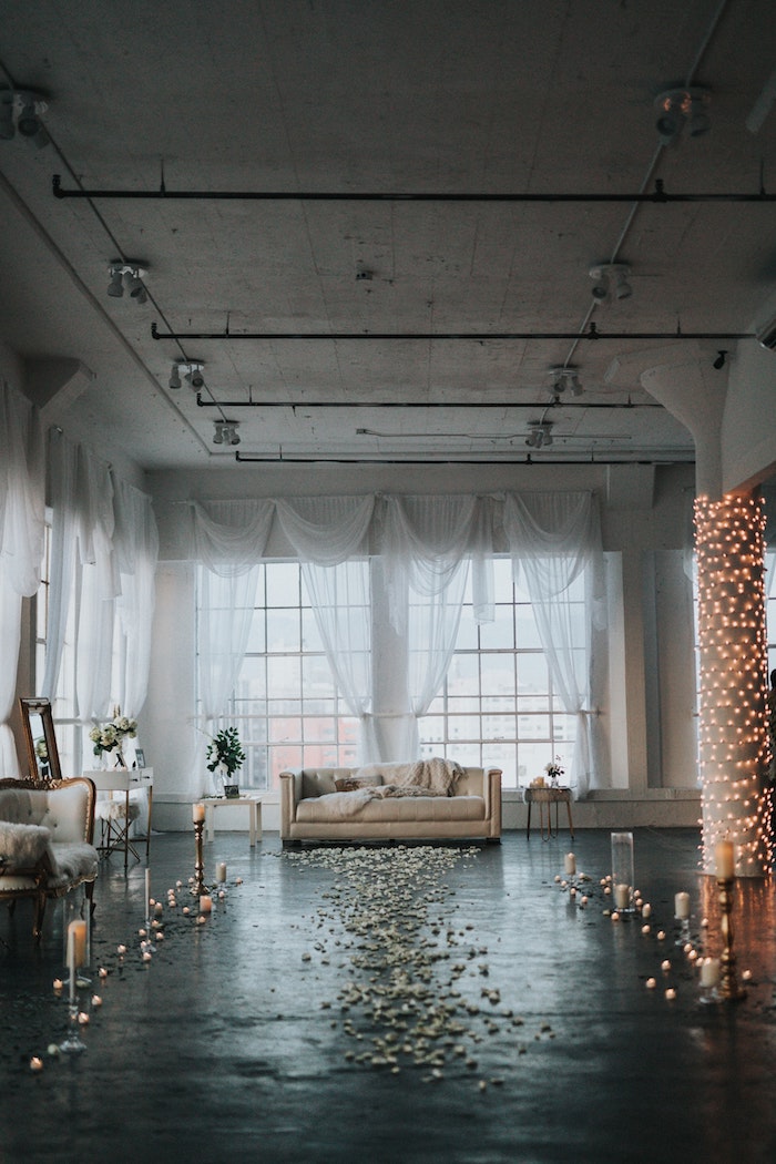 Salle de réception mariage, canapé beige, guirlandes lumineuses, bougies et pétales sur le sol, photo magnifique