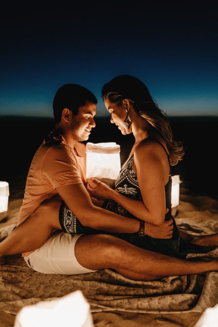 idée de sortie romantique en plein air, photo de jeune couple amoureux assis sur la sable avec lanternes en papier dans ses mains