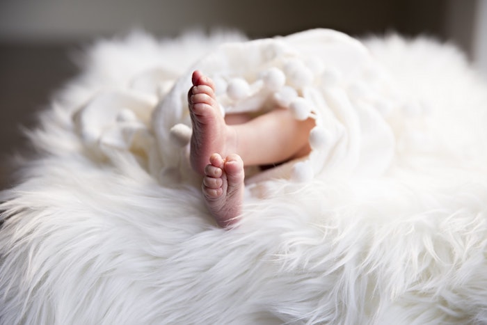 pieds d un bébé enveloppée d un plaid cocooning blanc sur un tapis blanc, lessive le chat bébé