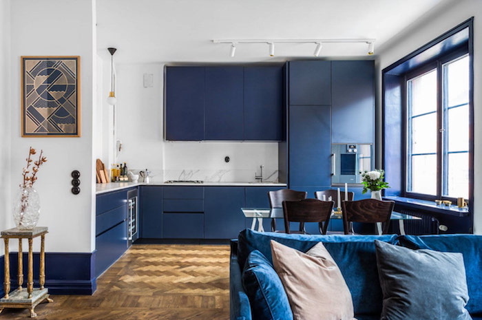 cuisine bleu nuit ouverte sur salon avec canapé bleu foncé, parquet bois, murs blancs et meuble hauts et bas bleu foncé de nuancier pantone