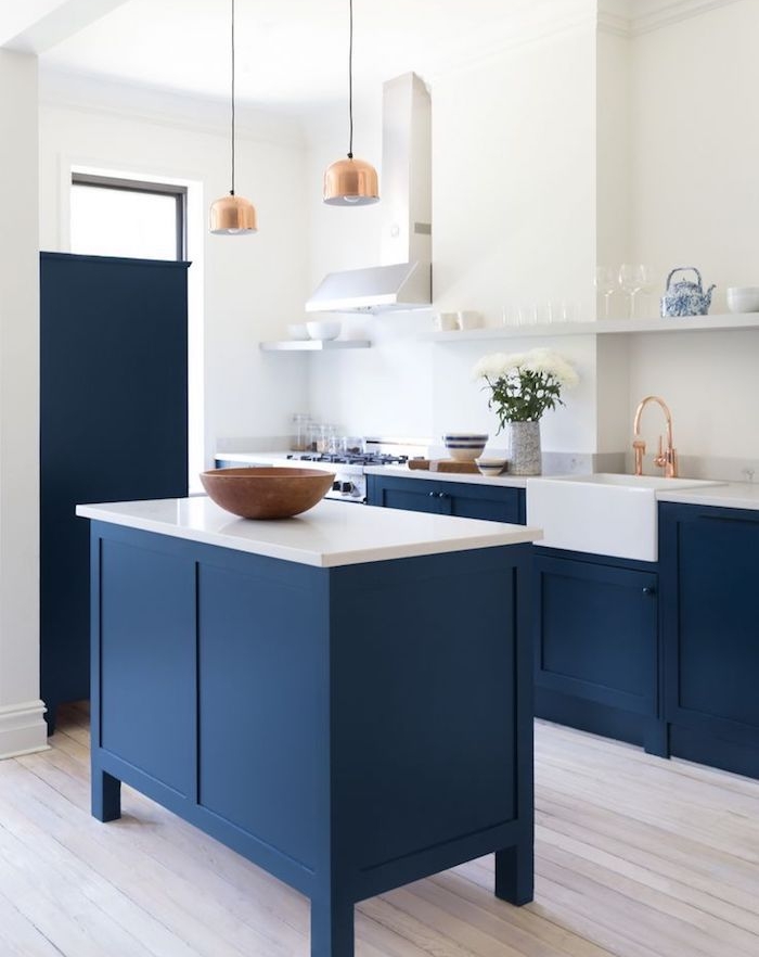 meuble bas et ilot central bleu dans cuisine blanche avec parquet clair et suspensions et robinetterie cuivre