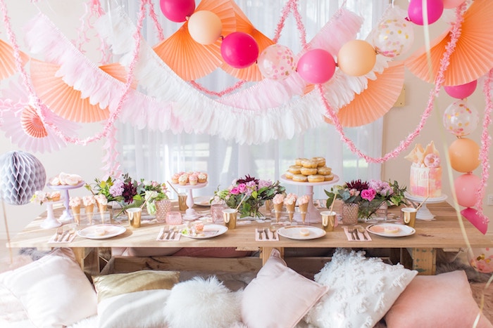decoration anniversaire boheme chic avec deco ballons, guirlande à éventails, table rustique chic décorée de fleurs, glace beignets et cucpakes, coussins boheme par sol