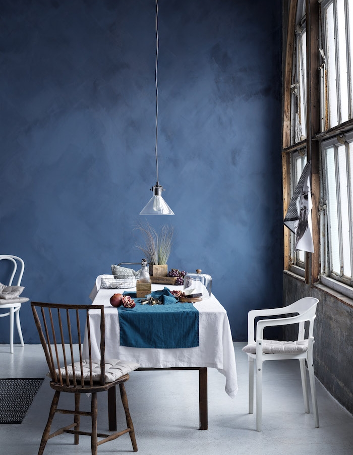salle à manger contemporaine en bleu foncé, sol et nappe blanche sur table de bois, grandes fenetres, suspension basse