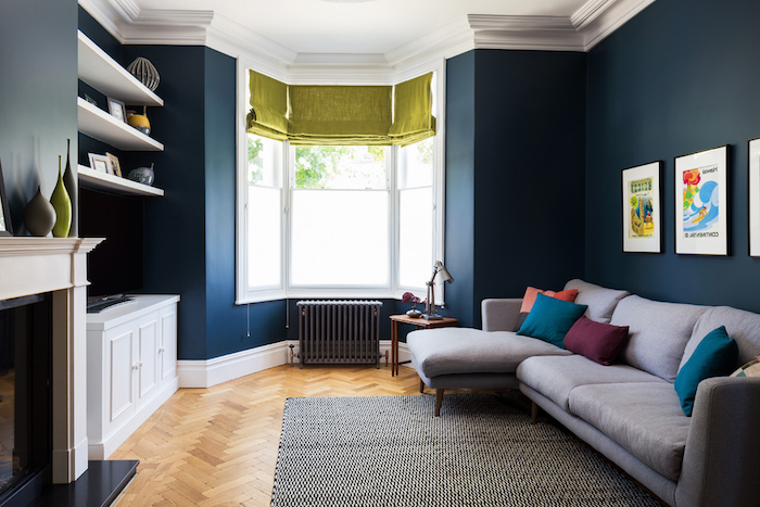 amenagement salon en longueur aux murs bleus et canapé gris décoré de coussins colorés, cheminée blanche, radiateur gris