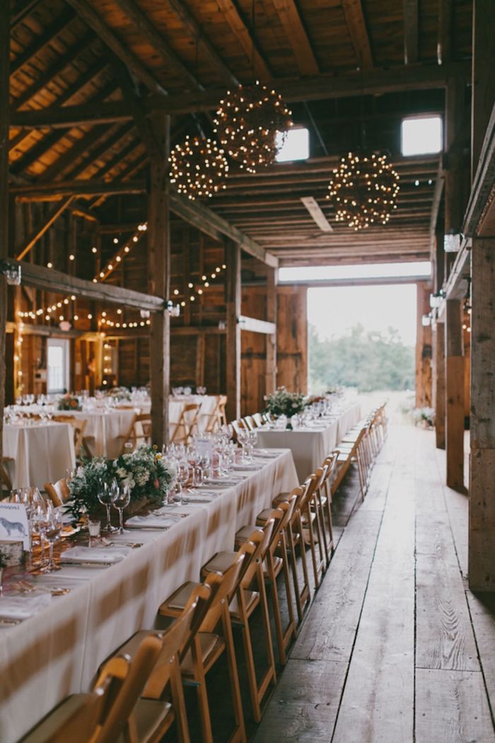 boules de guirlandes lumineuses pour decorer le plafond de vieilles granges rénovées, chaises bois, table avec nappe blanche, deco florale de mariage pour le centre