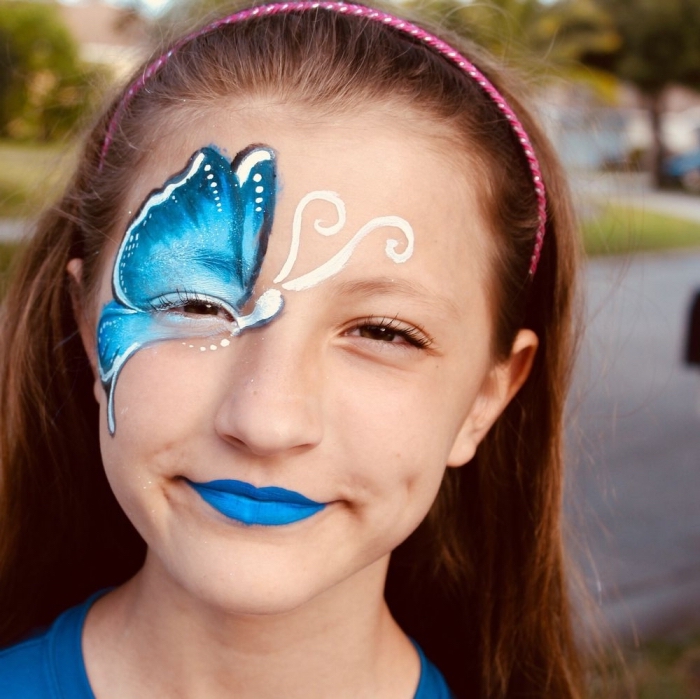 dessiner un masque de carnaval avec peinture faciale, modèle de papillon bleu aux ailes ombrées sur le visage d'une fille