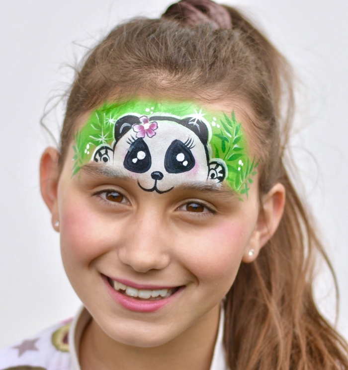 quel maquillage halloween facile pour enfant, dessin sur le front d'une petite fille à design mini panda avec fleur rose sur la tête caché dans l'herbe