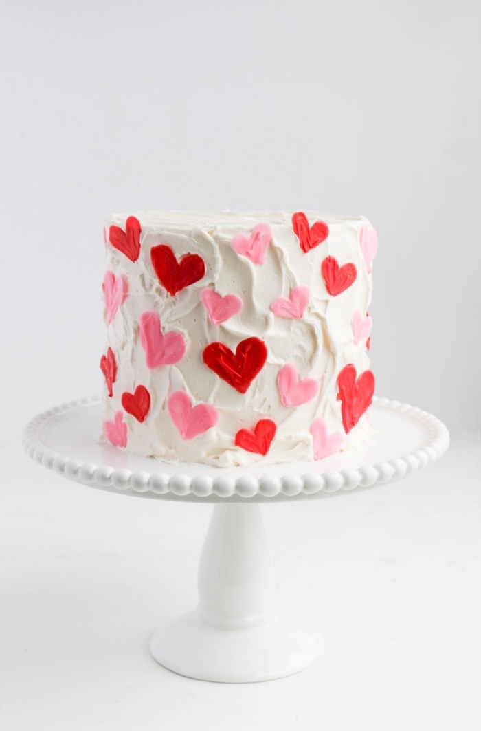 dessert fait maison pour un menu saint valentin romantique, modèle de gâteau rond au glaçage blanc avec coeurs décoratives rouges et roses