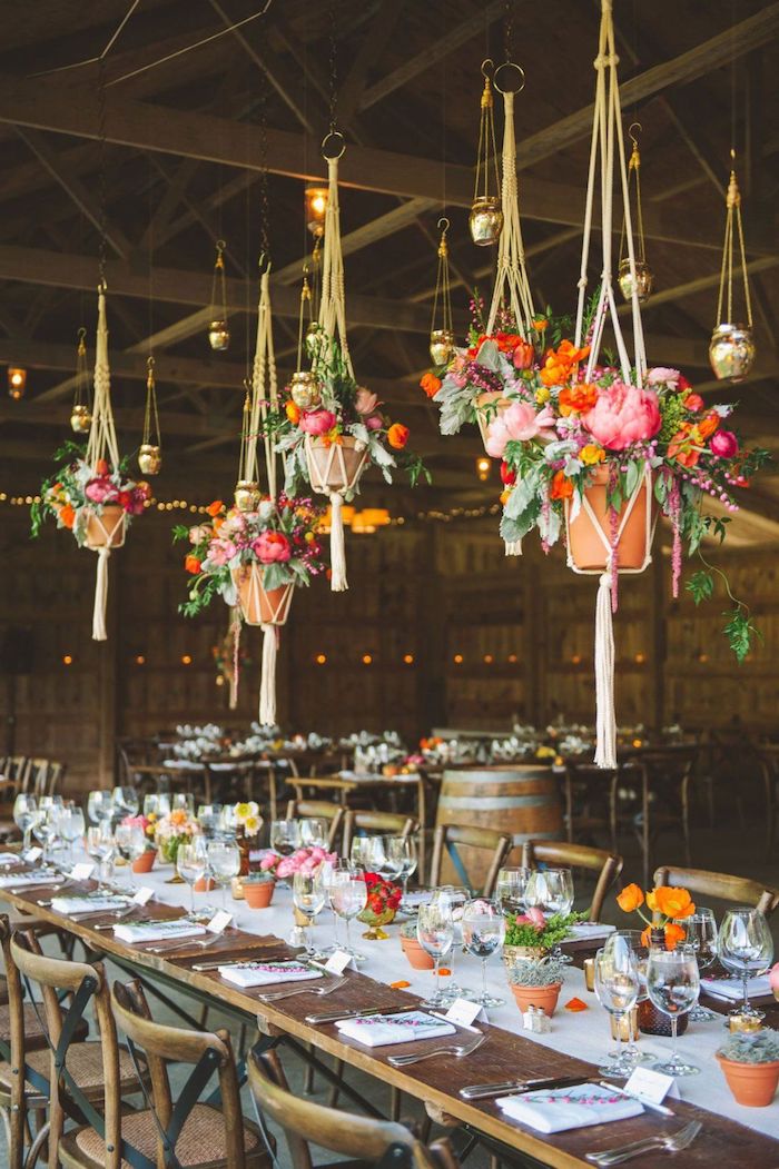 pots macramé suspendues avec des fleurs colorées au dessus de table et chaises bois, chemin de table blanc, petits pots de fleurs, idee deco mariage champetre chic