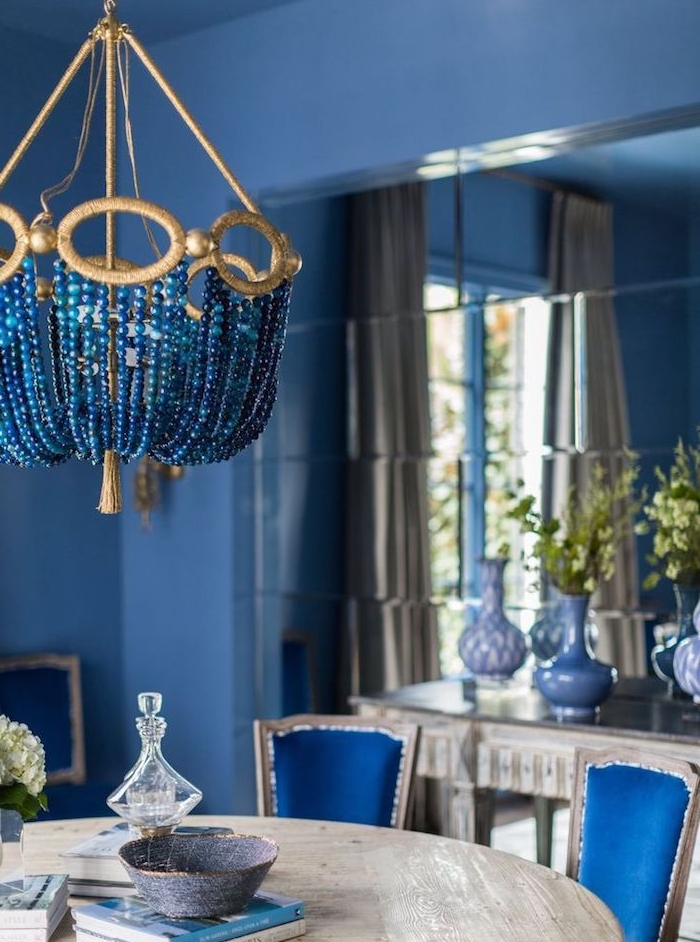 modele de salle a manger contemporaine aux murs bleus, table salle à manger bois brut, chaises bleues, vase avec des branches vertes