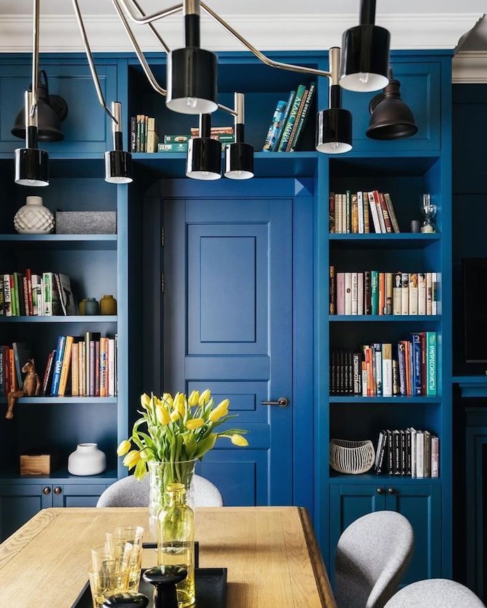 murs et porte de couleur bleue, petite bibliothèque à côté d une salle à manger avec table de bois et chaises grises