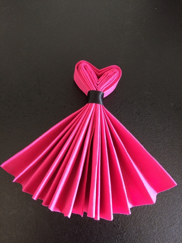exemple comment plier une serviette en papier rose fuchsia en forme de robe de princesse à l'aide d'un ruban noir