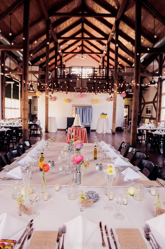 décoration de table mariage en petits soliflores sur nappe blanche, guirlande lumineuses pour décorer le plafond boisé avec poutres apparentes