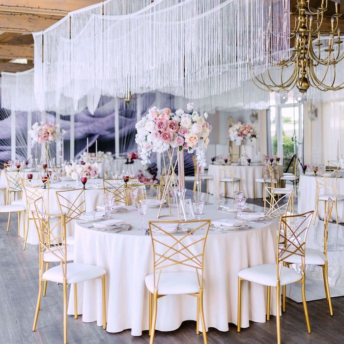 décorer le plafond mariage avec décoration chute de fils blancs au dessus de tables en nappes blanches entourées de chaises or et blanc avec bouquets de fleurs chic