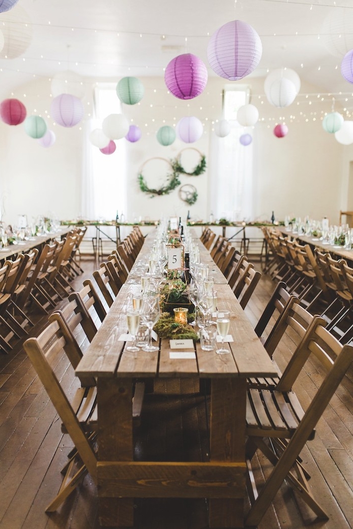 guirlande de lampions colorés géants et guirlande lumineuse en dessus, table et chaises bois brut, deco table mariage mousse florale et bougies