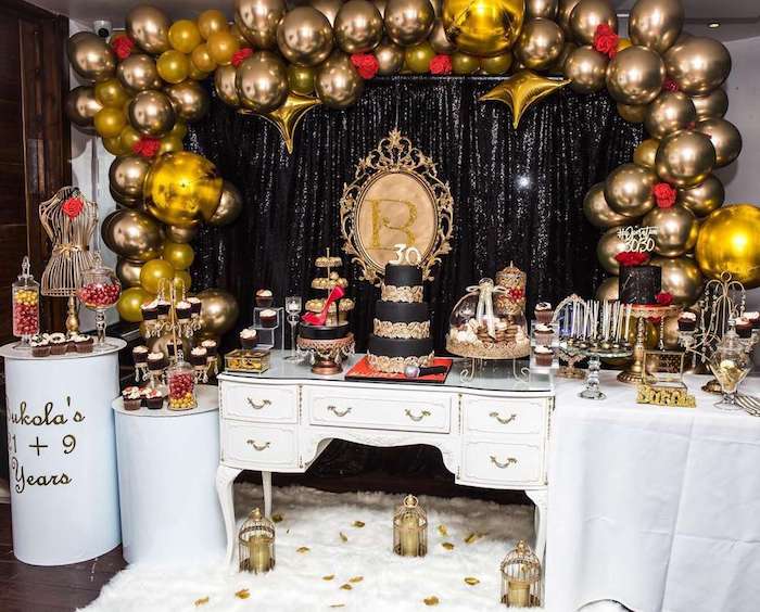 exemple theme anniversaire 30 ans arche de ballons dorés, rideau noir, cupcake, gateau et petites friandises or et noir