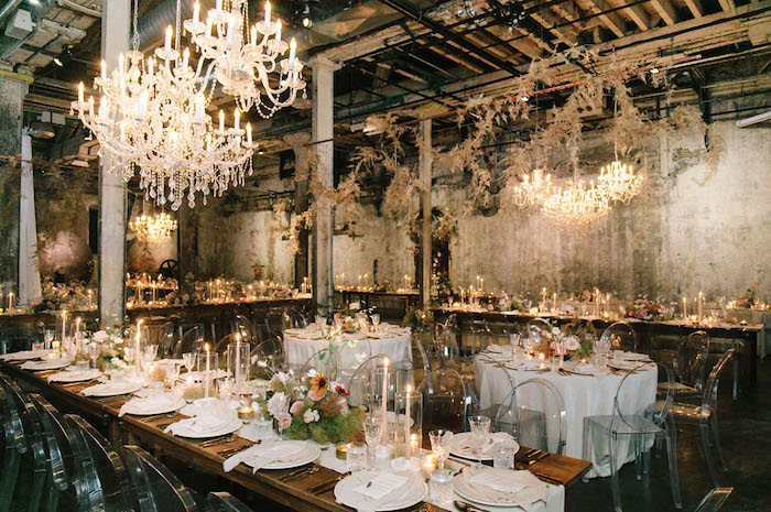 decoration industrielle de mariage dans salle de mariage aux murs bruts, lustres elegantes, chaises transparentes autour de table bois