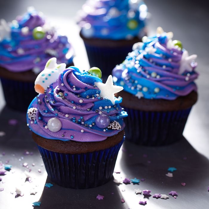 cupcakes maison au chocolat avec décoration crème au beurre motif galaxie de couleur bleu et violet et decoration billes colorées et étoiles