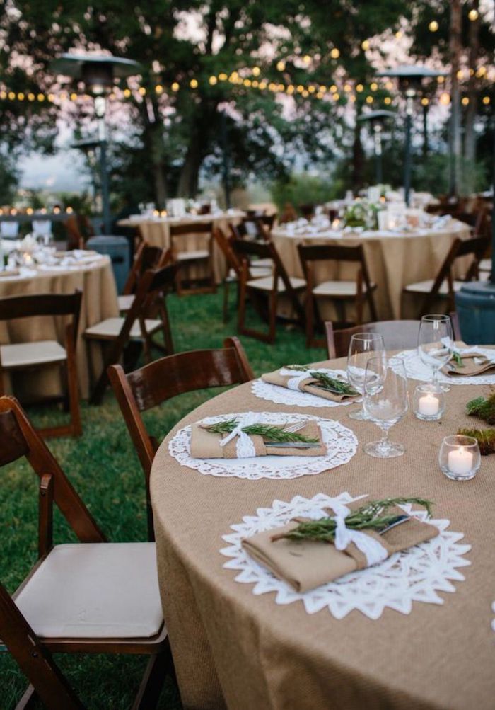 Table ronde avec nappe en lin et branches vertes sur les serviettes, guirlandes lumineuses decoration mariage champetre, décoration mariage champêtre 