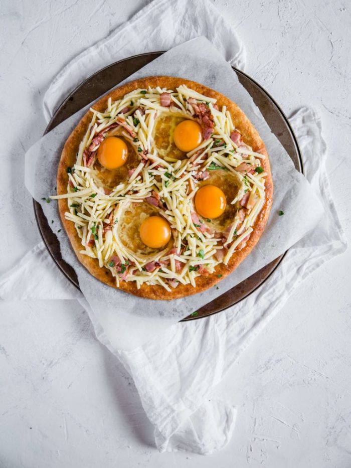 pizza sans gluten avec fromage, bacon et des oeufs cassés sur pâte à pizza sans gluten aux fromages, petit dejeuner ideal pizza maison