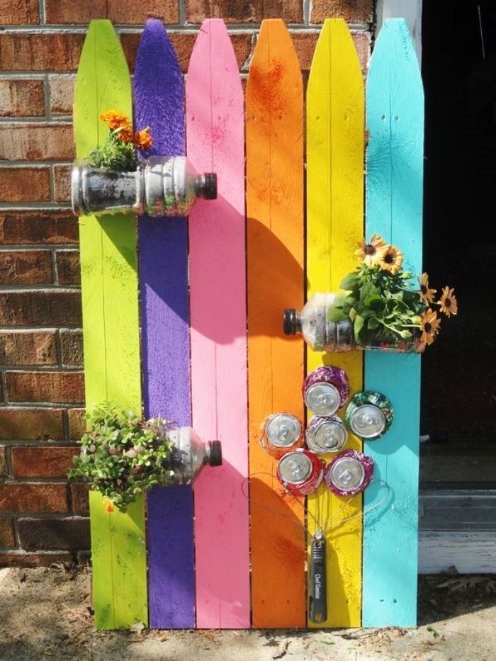 recyclage bouteilles en plastique transformées en pots de fleurs et une fleur en canettes de boisson recyclées sur mur de palette coloré