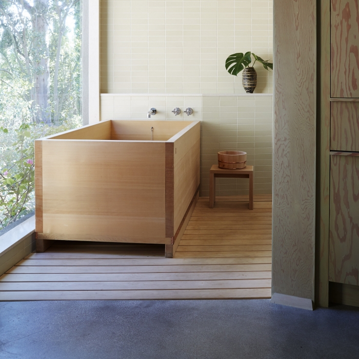 modèle de baignoire japonaise bois installée sur un tapis en bois clair, décoration salle de bain de style zen avec plantes et bois