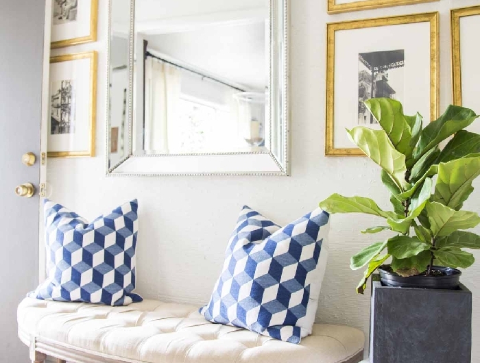 banquette coussin décoratif blanc et bleu pot fleur aspect béton mur de cadres dorés aménagement entrée maison interieur miroir