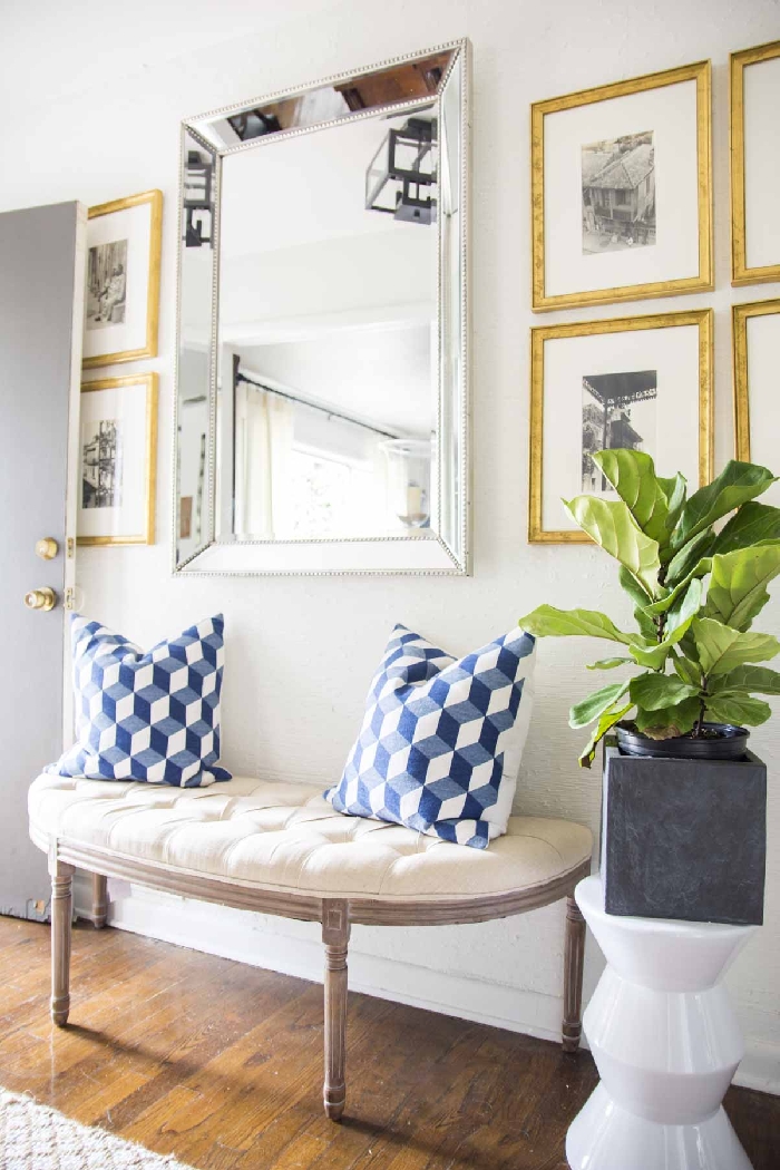 banquette coussin décoratif blanc et bleu pot fleur aspect béton mur de cadres dorés aménagement entrée maison interieur miroir