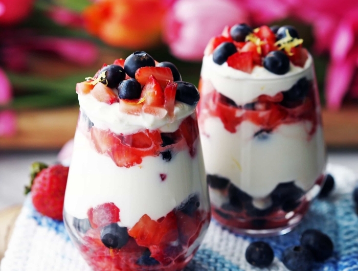 dessert leger aux fruits verre dessert yagourt et fruits fraîches fraises myrtilles planche bois dessert plateau serviette bleu et blanc fleurs tulipes