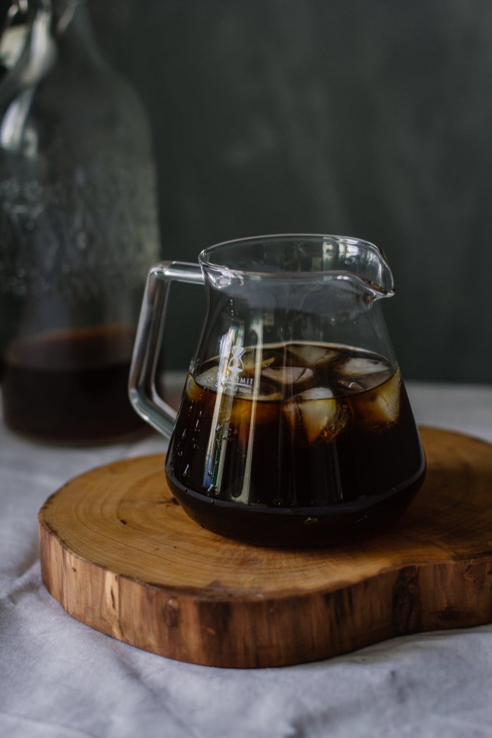 comment préparer un café glacé nespresso, recette de café noir froid pour l'été, verre de café noir avec glaçons sur tranche de bois