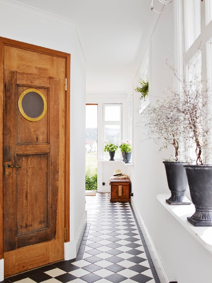 porte d entrée bois rustique déco couloir étroit carreaux sol blanc et noir coffre bois foncé pot de fleur béton vase murs blancs