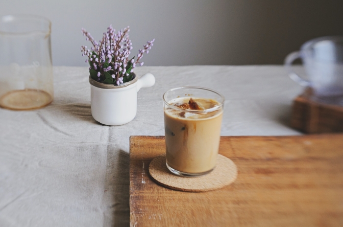 recette café glacé facile à réaliser soi-même, verre de café froid au lait et glaçons sur une plateau en bois et sous verre