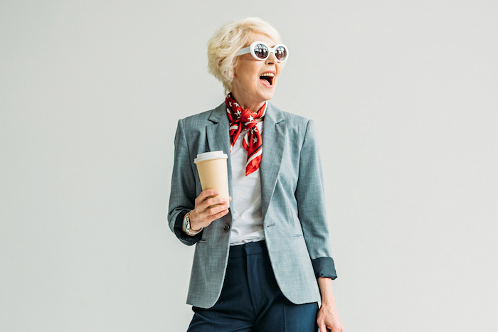exemple de coiffure femme 60 ans épanouie avec veste grise pantalon gris foncé fichu rouge lunettes de soleil monture blanche