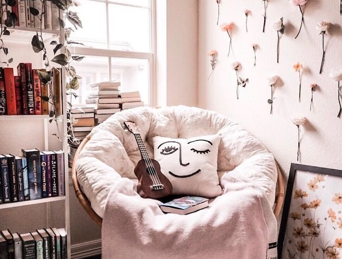 fauteuil confortable pour lire avec couverture gris clair et coussin à visage bibliothèque meuble blanc mur décoré de fleurs fraiche