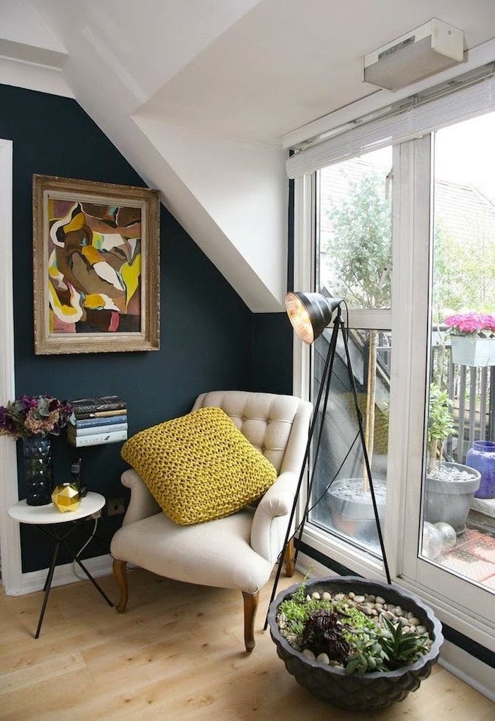 mur bibliothèque flottante petite taille avec fauteuil blanc cassé et mur bleu gris avec cadre art coloré et grand pot jardin interieur