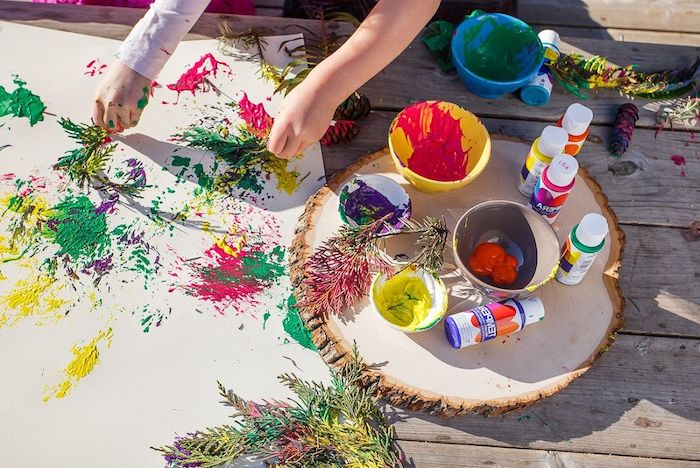 peinture enfant sur toile avec des branches de pin et des peintures de couleurs variées idee jeu en plein air enfant vacances été