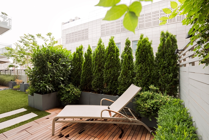 transat jardin aménagement petite terrasse en bois haie végétale conifère gros pots fleurs gris plantes vertes arbres mur végétal