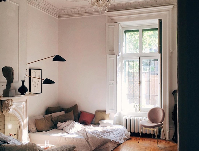 chambre à coucher dans interieur appartement parisien avec parquet chevron bois brut coussins colorés et matelas blanc murs blancs