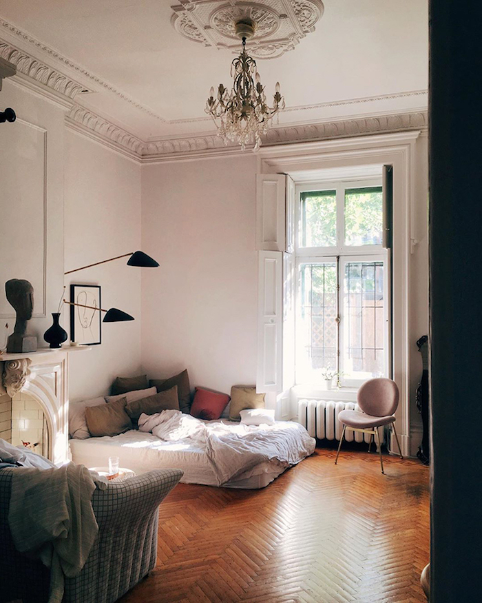chambre à coucher dans interieur appartement parisien avec parquet chevron bois brut coussins colorés et matelas blanc murs blancs