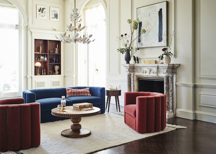 cheminée marbre fauteuil rouge forme arrondie canapé bleu table basse bois ronde tapis blanc murs blancs parquet marron foncé